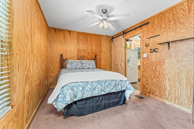 carpeted bedroom with wooden walls, white fridge with ice dispenser, ceiling fan, and a barn door