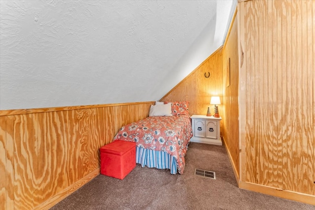 carpeted bedroom featuring wood walls, a textured ceiling, and vaulted ceiling