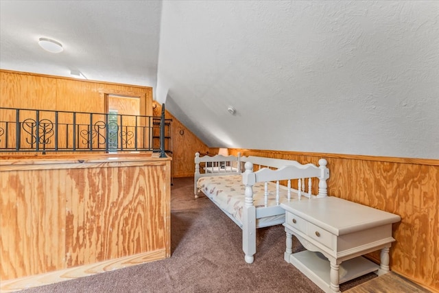 bedroom with carpet flooring, a textured ceiling, wood walls, and vaulted ceiling