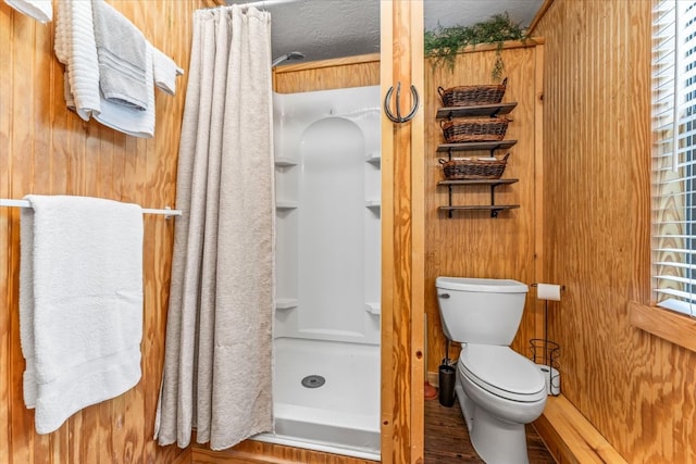 bathroom with a textured ceiling, wooden walls, hardwood / wood-style flooring, a shower with curtain, and toilet