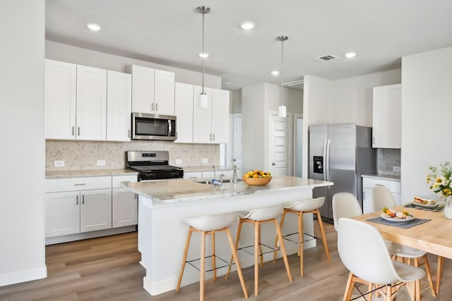 kitchen with a kitchen island with sink, white cabinets, hanging light fixtures, light wood-type flooring, and stainless steel appliances