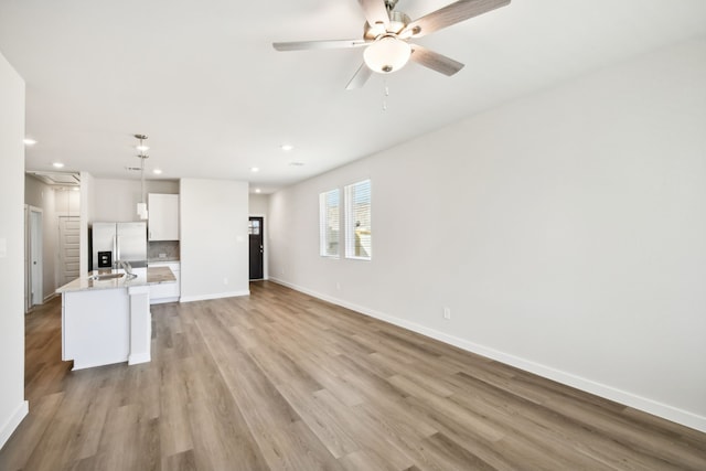 kitchen with an island with sink, white cabinets, hanging light fixtures, and stainless steel refrigerator with ice dispenser