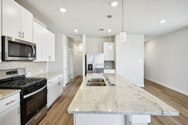 kitchen with a kitchen island with sink, decorative light fixtures, light hardwood / wood-style floors, white cabinetry, and stainless steel appliances