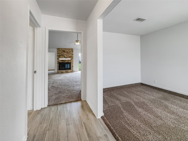 unfurnished room with light colored carpet, ceiling fan, and a fireplace