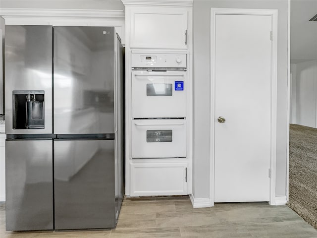 kitchen with stainless steel fridge with ice dispenser, light hardwood / wood-style floors, white cabinets, and double oven