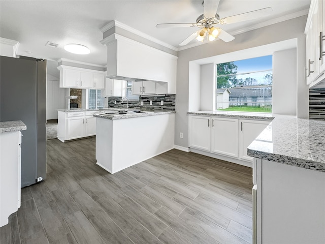 kitchen with white cabinets, light hardwood / wood-style flooring, stainless steel fridge, kitchen peninsula, and ceiling fan