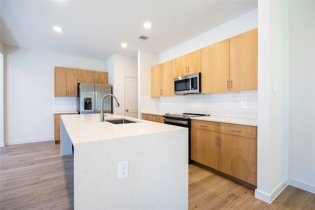 kitchen featuring light wood-type flooring, appliances with stainless steel finishes, a center island with sink, and sink