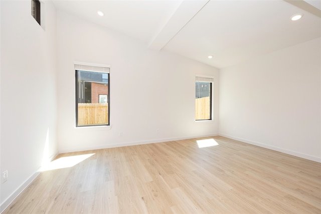 spare room featuring lofted ceiling, light hardwood / wood-style floors, and a healthy amount of sunlight