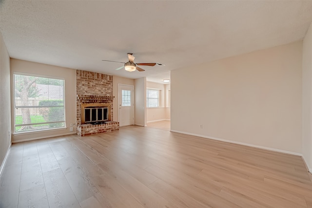 unfurnished living room with a textured ceiling, ceiling fan, light wood-type flooring, and a brick fireplace