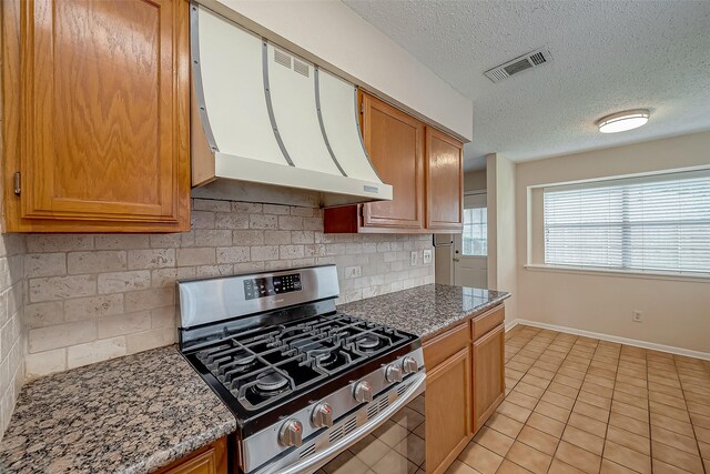 kitchen with a textured ceiling, stainless steel gas range oven, backsplash, light stone countertops, and custom range hood