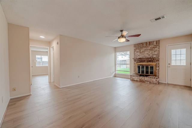 unfurnished living room featuring a healthy amount of sunlight, a brick fireplace, ceiling fan, and light hardwood / wood-style floors