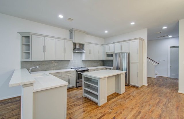 kitchen featuring kitchen peninsula, wall chimney exhaust hood, light hardwood / wood-style flooring, stainless steel appliances, and a center island