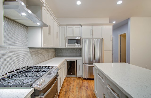 kitchen featuring appliances with stainless steel finishes, light wood-type flooring, wall chimney exhaust hood, and white cabinetry