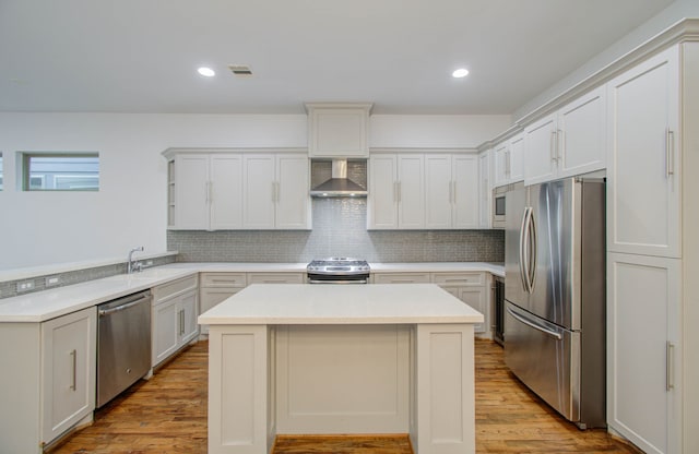 kitchen featuring wall chimney exhaust hood, a center island, light hardwood / wood-style floors, and appliances with stainless steel finishes