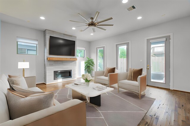 living room with a large fireplace, light hardwood / wood-style flooring, and ceiling fan