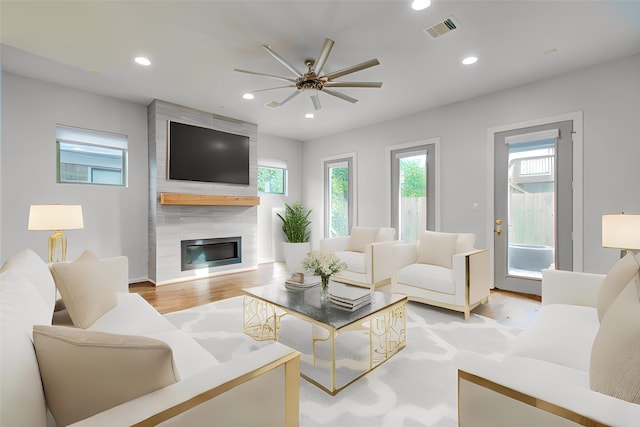 living room featuring ceiling fan, light hardwood / wood-style flooring, and a large fireplace