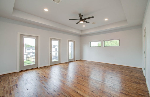 unfurnished room featuring hardwood / wood-style flooring, a raised ceiling, ceiling fan, and plenty of natural light