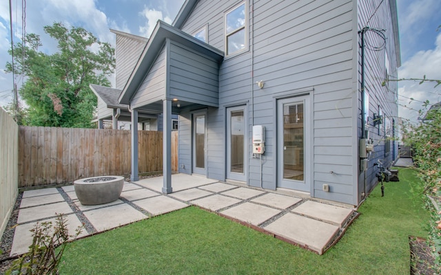 rear view of property featuring a patio, a yard, and a fire pit