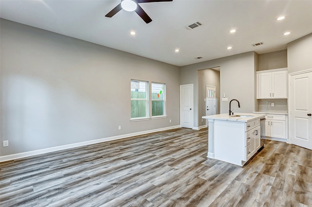 kitchen with light hardwood / wood-style floors, white cabinetry, sink, an island with sink, and ceiling fan