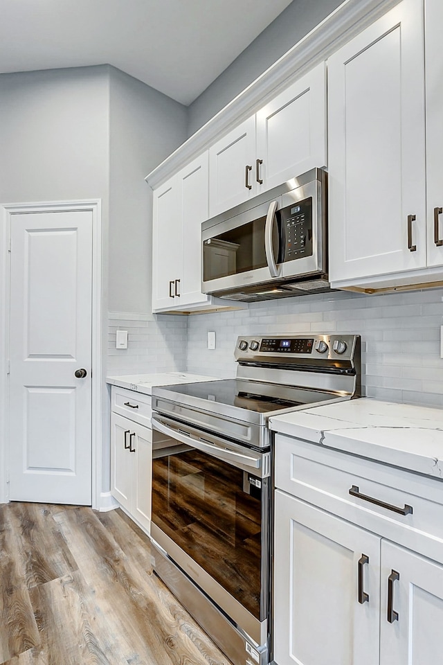 kitchen with white cabinetry, stainless steel appliances, light stone counters, decorative backsplash, and light hardwood / wood-style floors