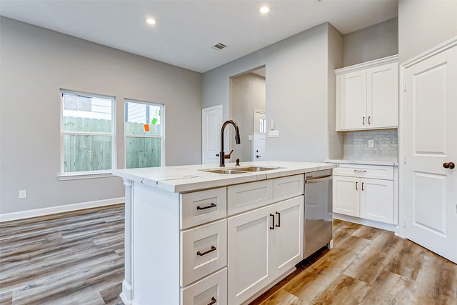 kitchen featuring light wood-type flooring, light stone counters, white cabinetry, sink, and a center island with sink