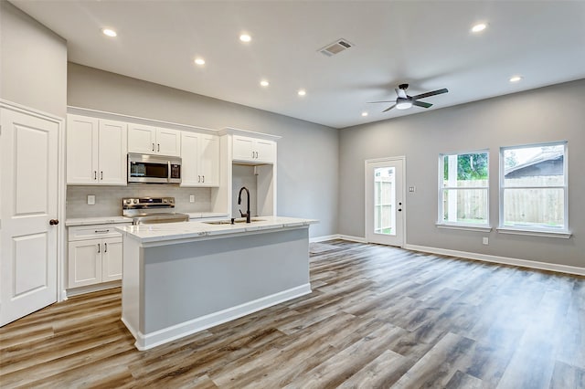 kitchen with hardwood / wood-style floors, stainless steel appliances, sink, ceiling fan, and a center island with sink