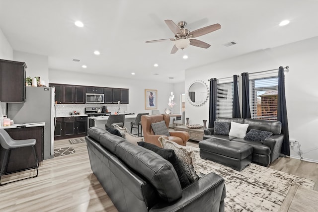 living room with ceiling fan, sink, and light wood-type flooring