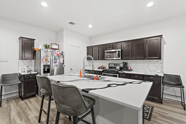 kitchen with light wood-type flooring, a kitchen breakfast bar, sink, appliances with stainless steel finishes, and a center island with sink