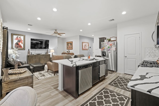 kitchen featuring sink, ceiling fan, appliances with stainless steel finishes, a center island with sink, and light hardwood / wood-style floors