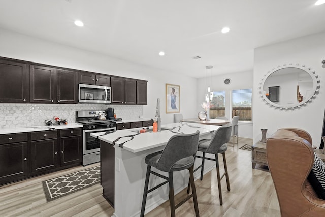 kitchen featuring light wood-type flooring, stainless steel appliances, a kitchen breakfast bar, hanging light fixtures, and a center island with sink