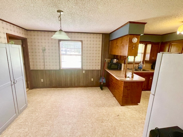 kitchen with wood walls, a textured ceiling, hanging light fixtures, and white refrigerator