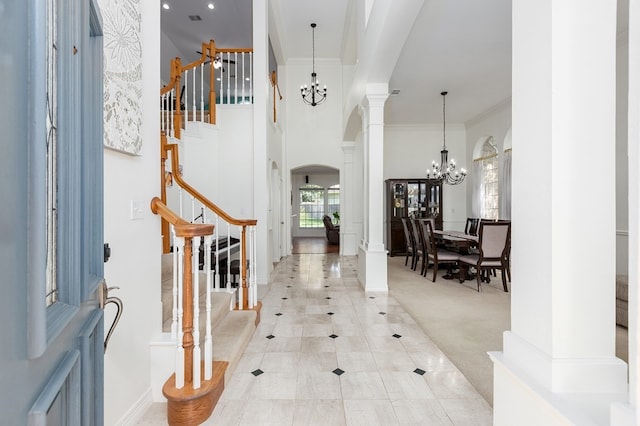 foyer entrance featuring light carpet, ornate columns, ornamental molding, a chandelier, and a towering ceiling