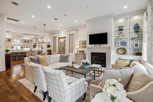 living room with visible vents, a chandelier, dark wood-type flooring, and a glass covered fireplace