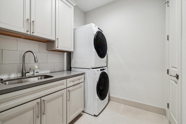 clothes washing area with stacked washer / dryer, a sink, cabinet space, and baseboards