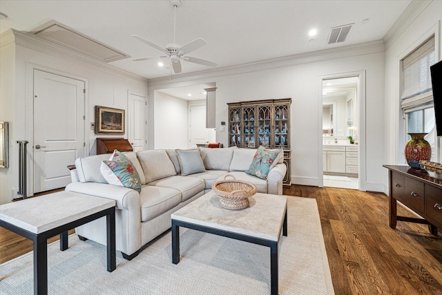 living area featuring attic access, visible vents, a ceiling fan, ornamental molding, and wood finished floors