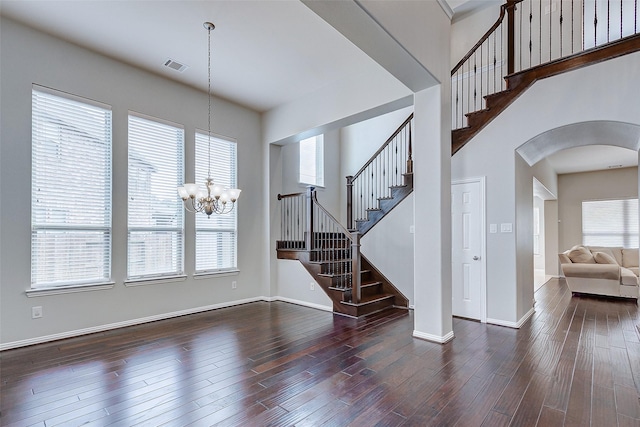 unfurnished living room with visible vents, stairway, an inviting chandelier, wood finished floors, and arched walkways