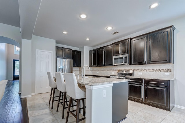 kitchen featuring visible vents, arched walkways, a sink, decorative backsplash, and appliances with stainless steel finishes