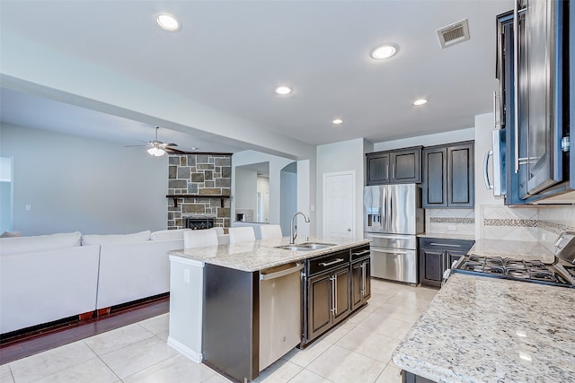 kitchen featuring stainless steel appliances, sink, a stone fireplace, ceiling fan, and a kitchen island with sink