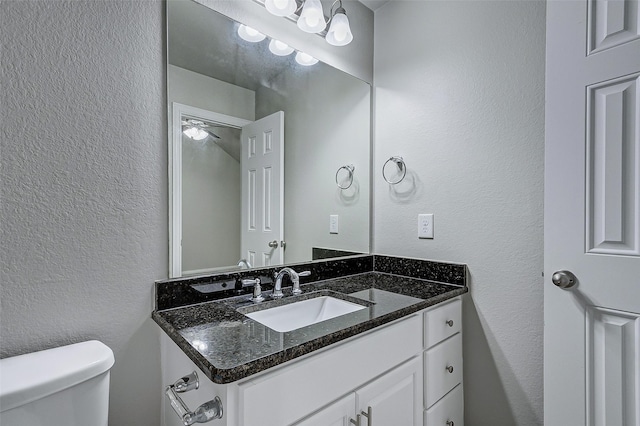 bathroom featuring vanity, toilet, and a textured wall