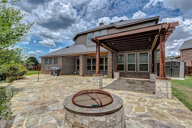 rear view of house with brick siding, an outdoor fire pit, a storage shed, an outbuilding, and a patio