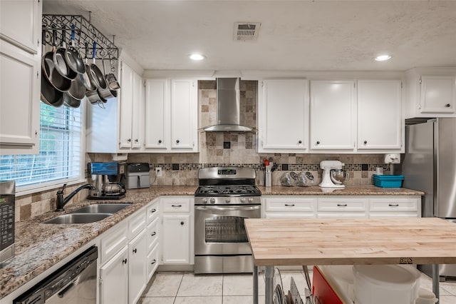 kitchen featuring white cabinets, appliances with stainless steel finishes, sink, wall chimney exhaust hood, and butcher block counters