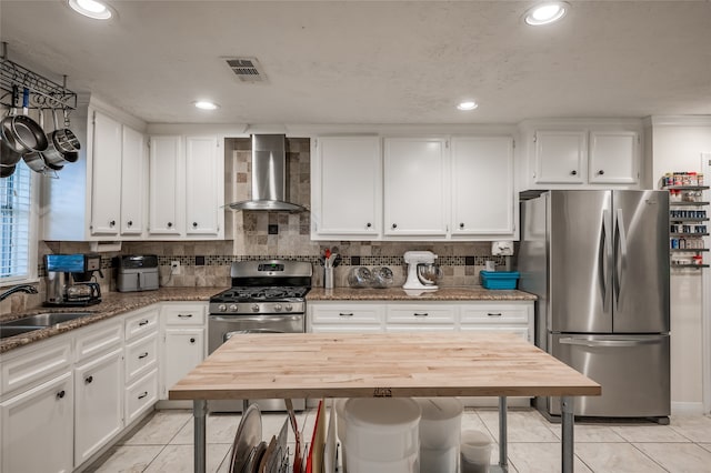 kitchen with white cabinetry, light tile patterned floors, stainless steel appliances, wood counters, and wall chimney range hood