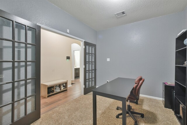 carpeted office with a textured ceiling and french doors