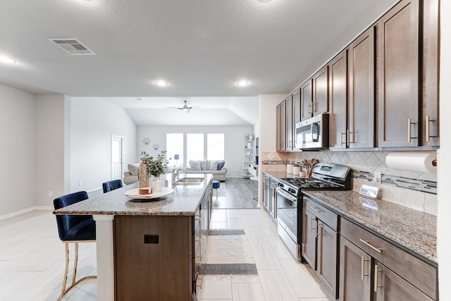 kitchen featuring light stone countertops, stainless steel appliances, ceiling fan, a kitchen bar, and a center island with sink