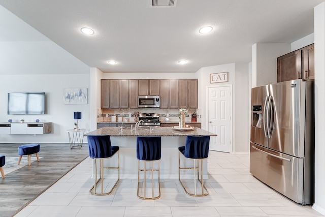 kitchen featuring a breakfast bar area, a center island with sink, light hardwood / wood-style flooring, stone countertops, and appliances with stainless steel finishes