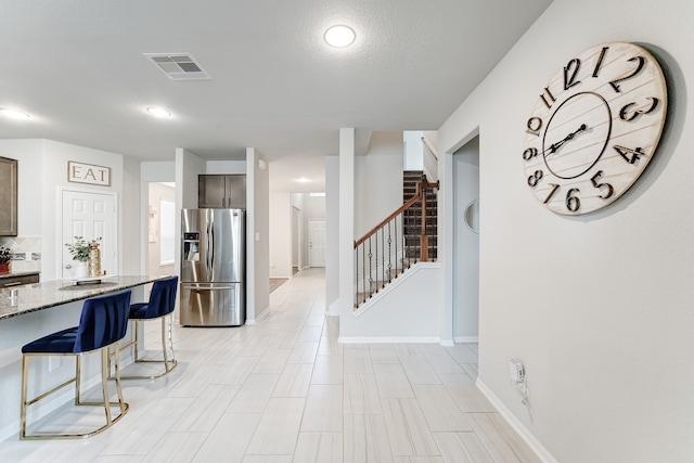 interior space featuring a breakfast bar area, light stone counters, a textured ceiling, and stainless steel refrigerator with ice dispenser