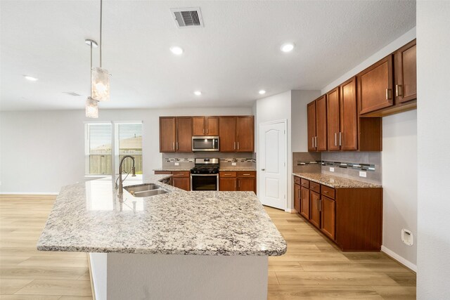 kitchen featuring light wood-type flooring, stainless steel appliances, an island with sink, sink, and hanging light fixtures