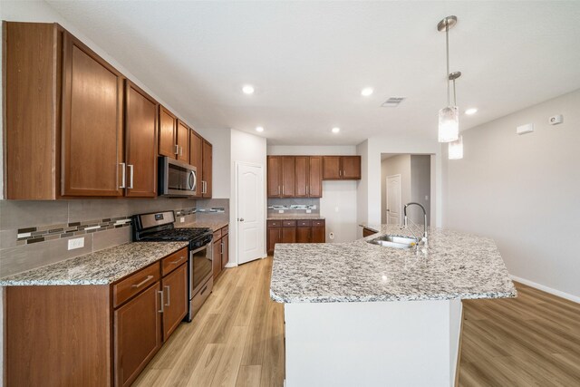 kitchen featuring light wood-type flooring, stainless steel appliances, a center island with sink, and sink