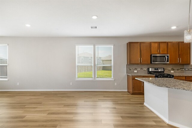 kitchen featuring decorative light fixtures, light stone countertops, appliances with stainless steel finishes, light hardwood / wood-style floors, and decorative backsplash