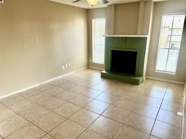 unfurnished living room featuring a wealth of natural light, ceiling fan, light tile patterned floors, and a brick fireplace